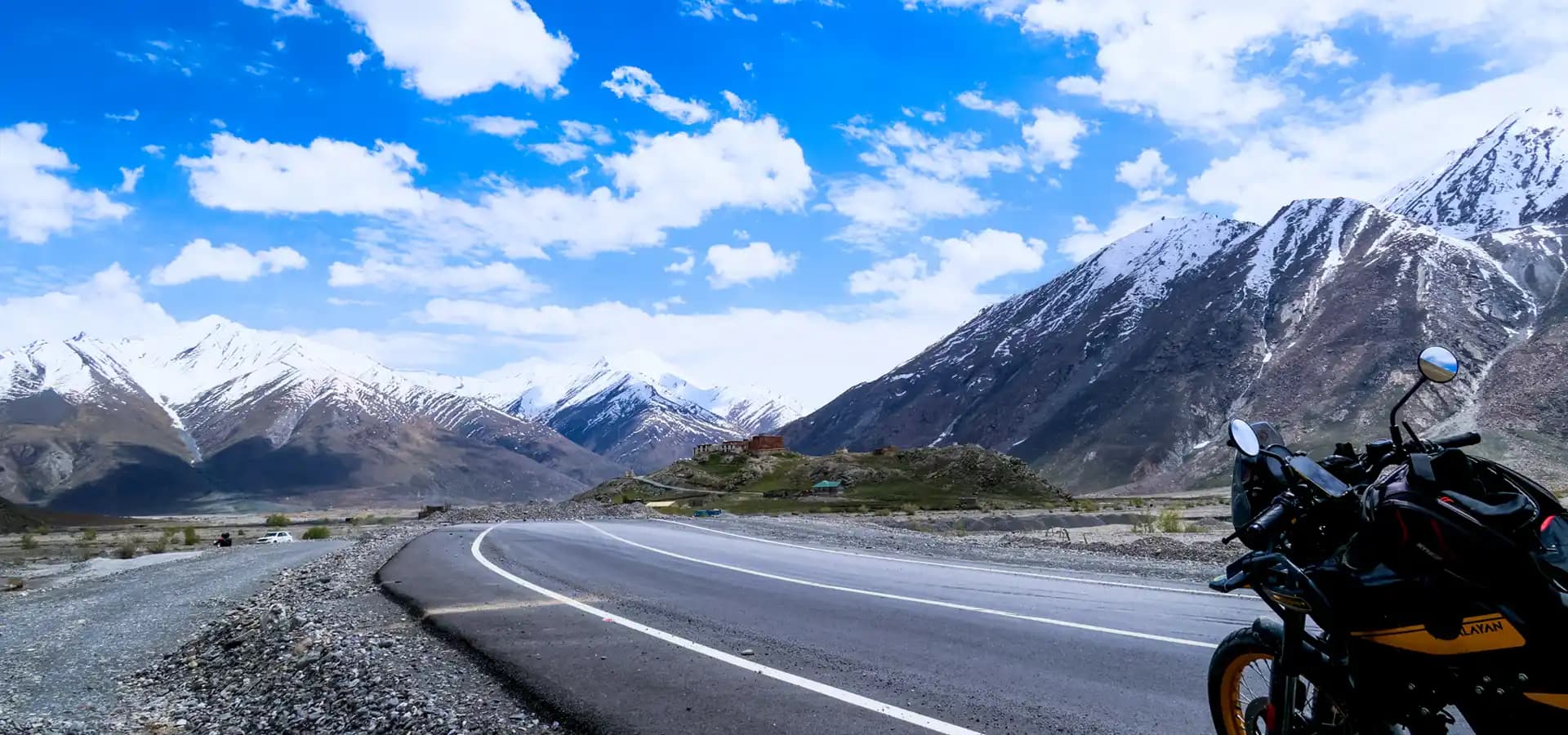 Indian Rides – Motorreis door de Himalaya van Ladakh Indian Rides motorfiets op een bergweg in Ladakh met besneeuwde Himalayabergen op de achtergrond